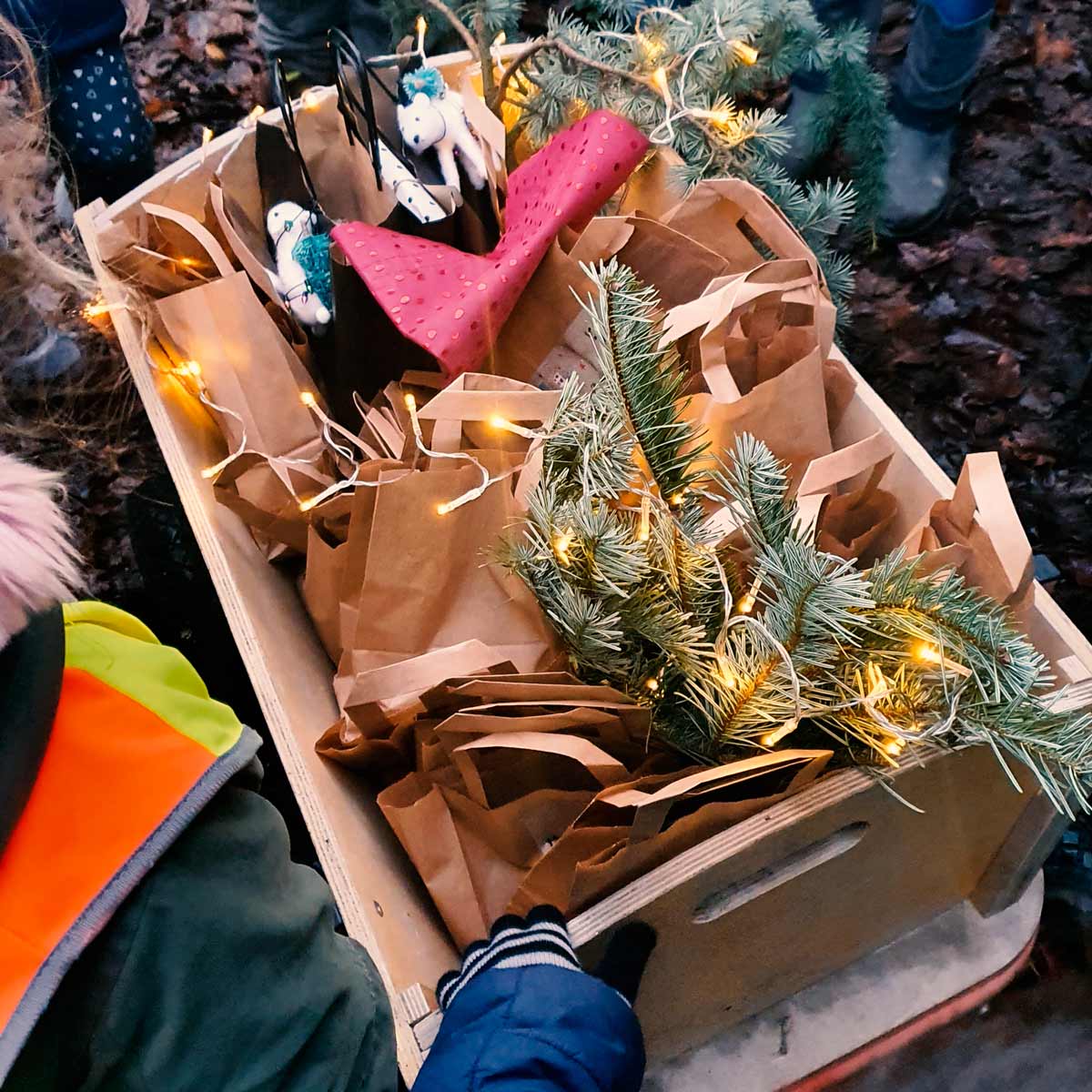 Ein Bollerwagen mit Geschenktüten, Tannenzweigen und einer Lichterkette.