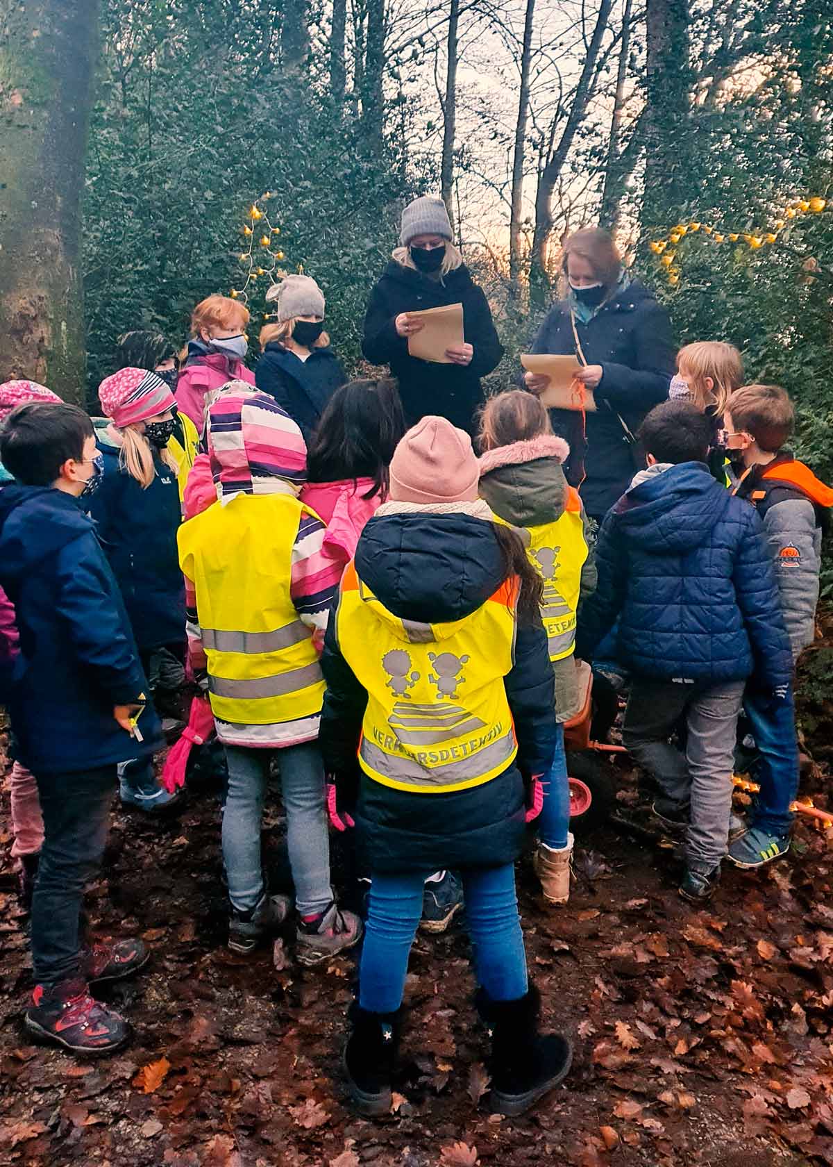 Zwei Erwachsene, die einer Kindergruppe im Wald etwas vorlesen.