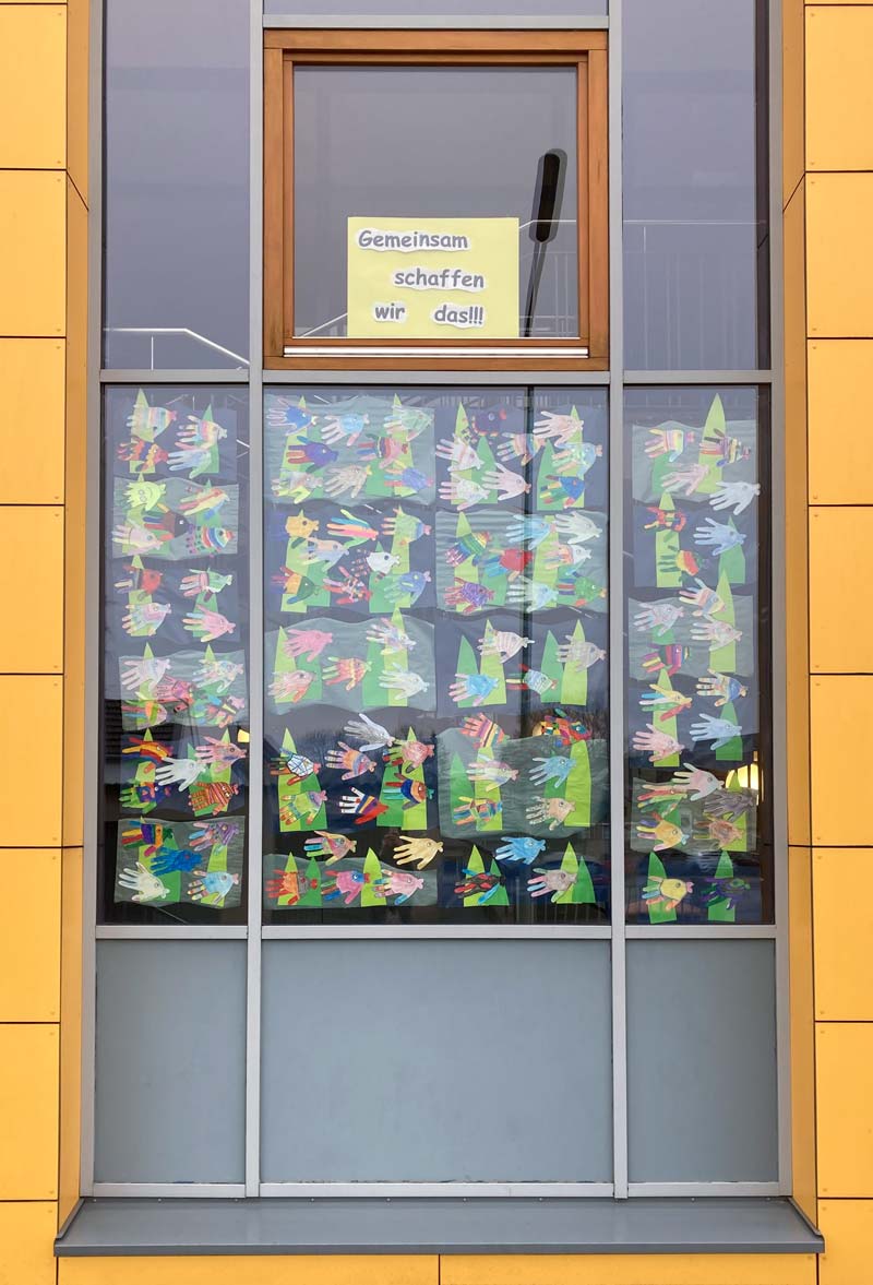 Fensterfront mit vielen gestalteten Fischbildern und einem Plakat mit der Aufschrift: Gemeinsam schaffen wir das!!!