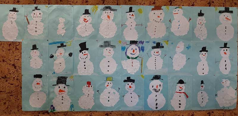 Von Kindern gestaltete Schneemannbilder in drei Reihen an einer Korkwand.