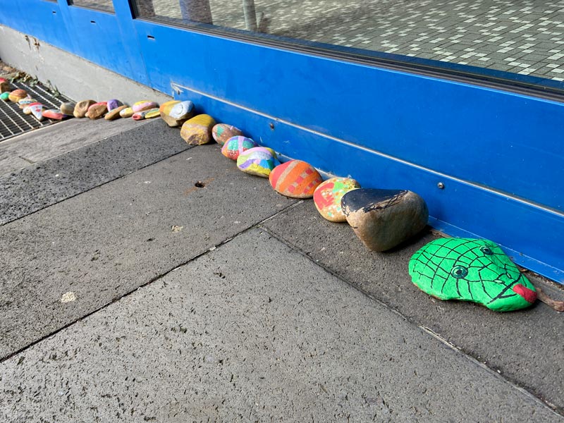 Bunt bemalte Steine als Schlange hintereinander gelegt auf dem Boden.