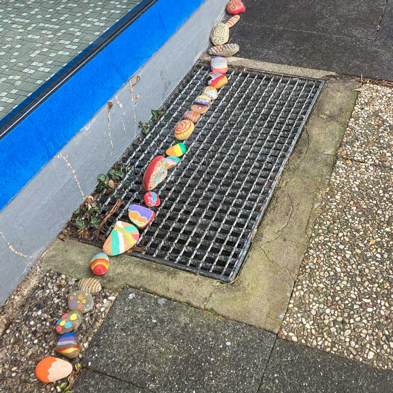 Bunt bemalte Steine als Schlange hintereinander gelegt auf dem Boden.