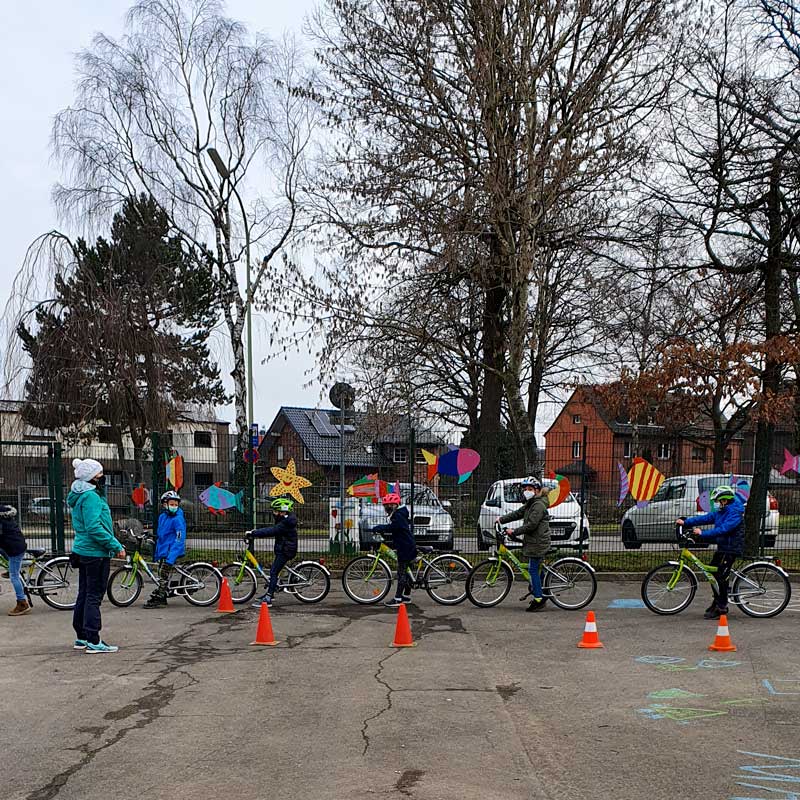 Kinder mit Masken und Helmen sitzen auf ihren Fahrrädern und bilden eine lange Schlange.