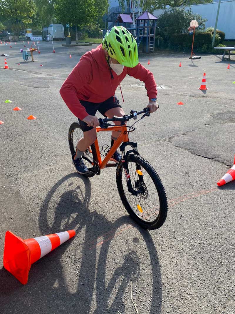 Fahrradfahrer mit Helm auf dem Schulhof mit Parcours im Hintergrund.