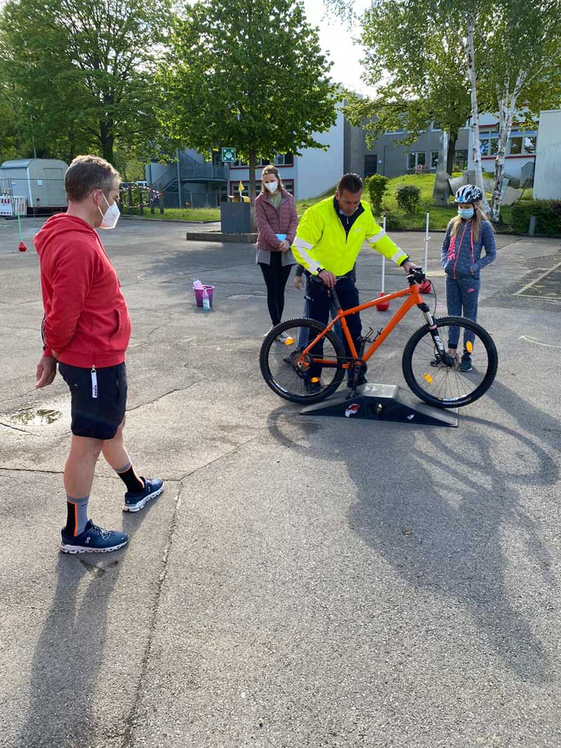 Polizist schiebt ein Fahrrad über eine Minirampe und wird von drei Personen beobachtet.
