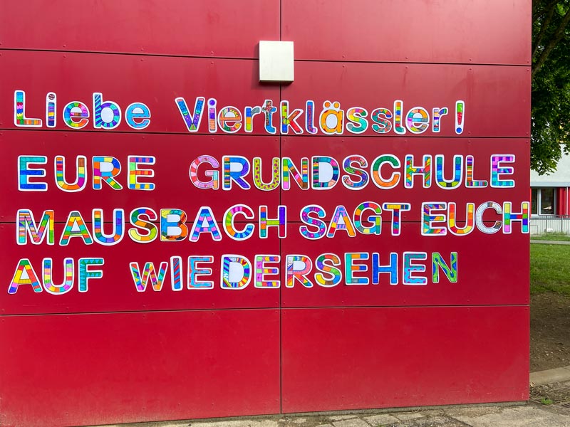 Eine rote Wand mit ausgeschnittenen Buchstaben: Liebe Viertklässler! Eure Grundschule Mausbach sagt euch auf Wiedersehen.