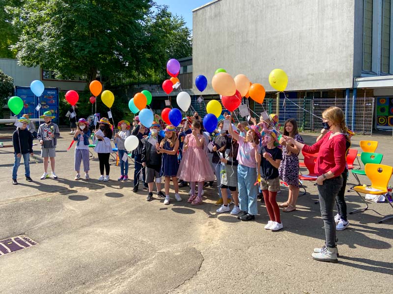 Eine Gruppe von Schulkindern und Lehrerin halten bunte Luftballons in der Hand.