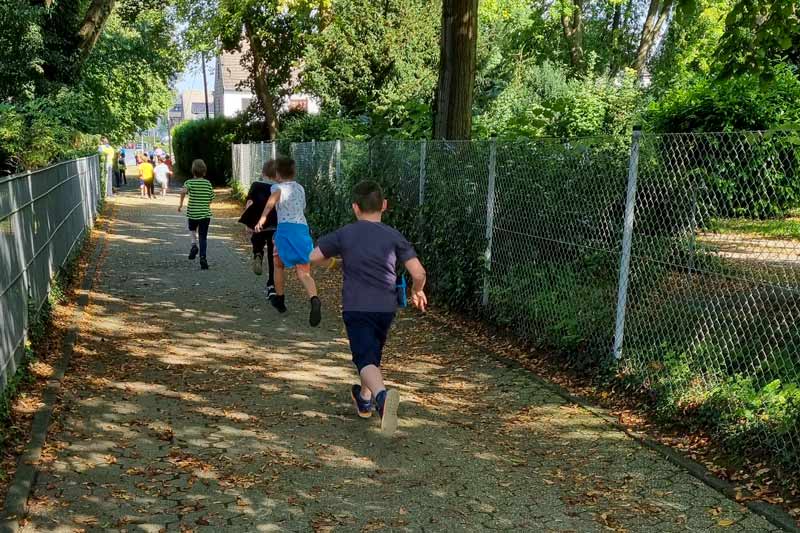 Eine Kindergruppe von hinten beim Laufen auf einem Gehweg.