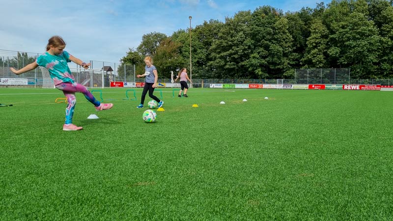 Drei Mädchen beim Fußballtraining auf einem Kunstrasenplatz.