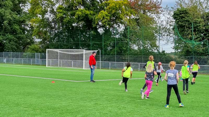 Mädchen mit Trainer bei einem Trainingsspiel auf dem Fußballplatz.