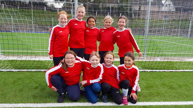 Neun Mädchen in roten Trikots beim Gruppenbild auf dem Fußballplatz.