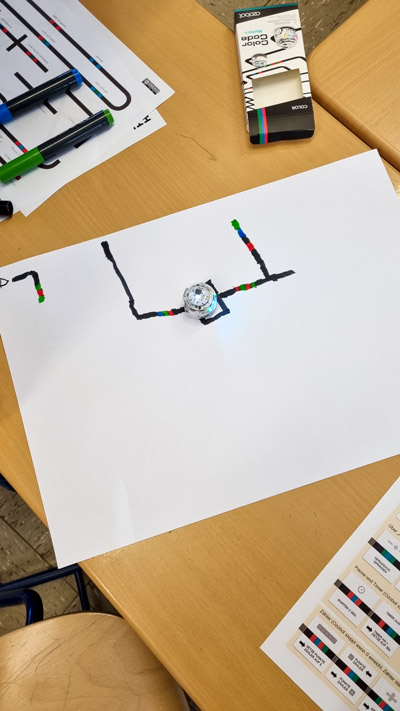 Farbige Programmierskizzen mit Minirobotern liegen auf den Klassentischen.