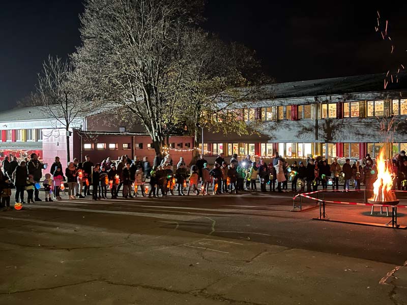 Schulkinder mit Laternen vor dem Schulgebäude stehen am Martinsfeuer.