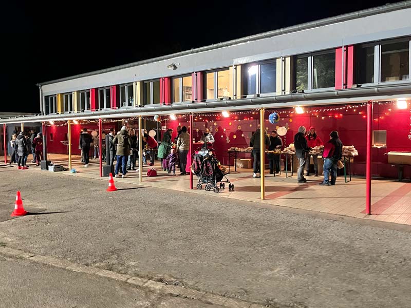 Mit Lichterketten dekorierter Verkaufsstand mit Besuchern auf dem Schulhof.