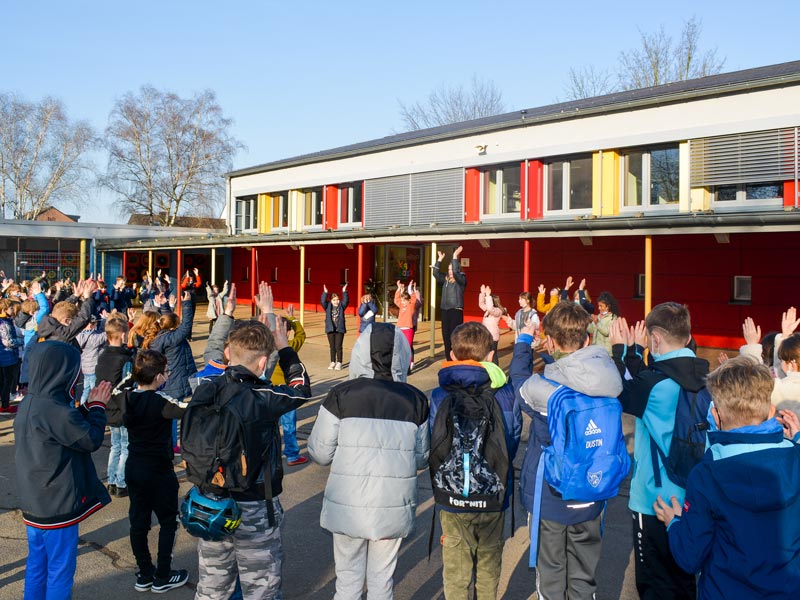 Eine große Kindergruppe auf dem Schulhof klatscht mit der Lehrerin.