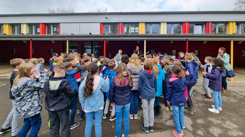 Eine Kindergruppe auf dem Schulhof verfolgt ein Konzert von zwei Musiker*innen.