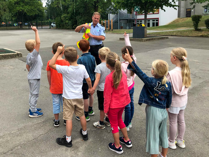 Kinder, die auf dem Schulhof stehen und die Fragen eines Polizisten beantworten.
