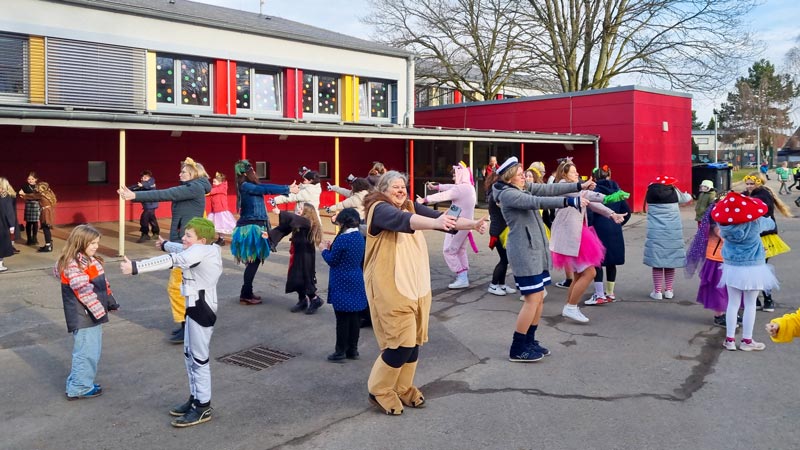 Verkleidete Kinder und Lehrer*innen tanzen auf dem Schulhof.