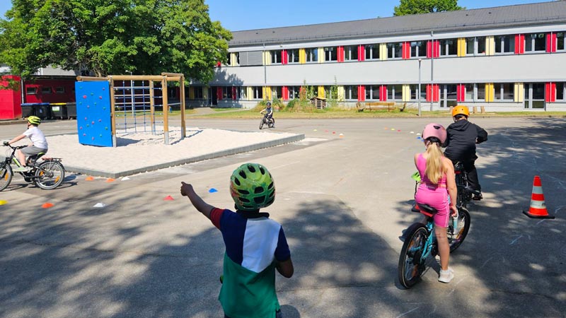 Schulkinder mit Fahrrädern und Helmen fahren ein Parcours auf dem Schulhof.