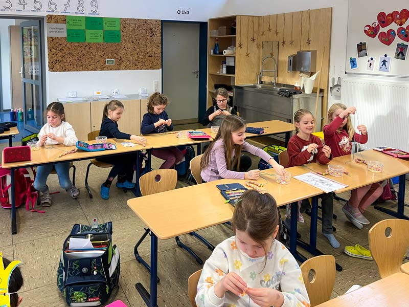 Schülerinnen basteln im Klassenzimmer an ihren Tischen.