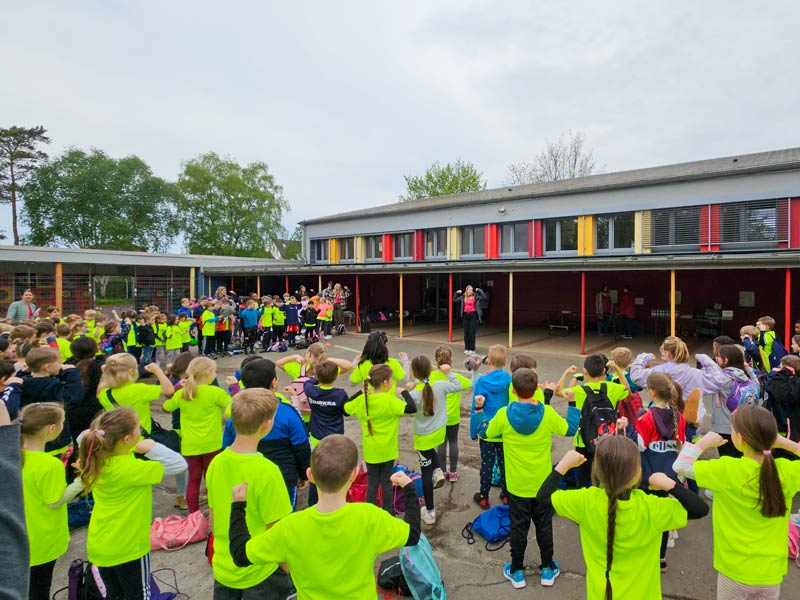 Schüler und Schülerinnen mit gelben T-Shirts stehen im Halbkreis auf dem Schulhof.