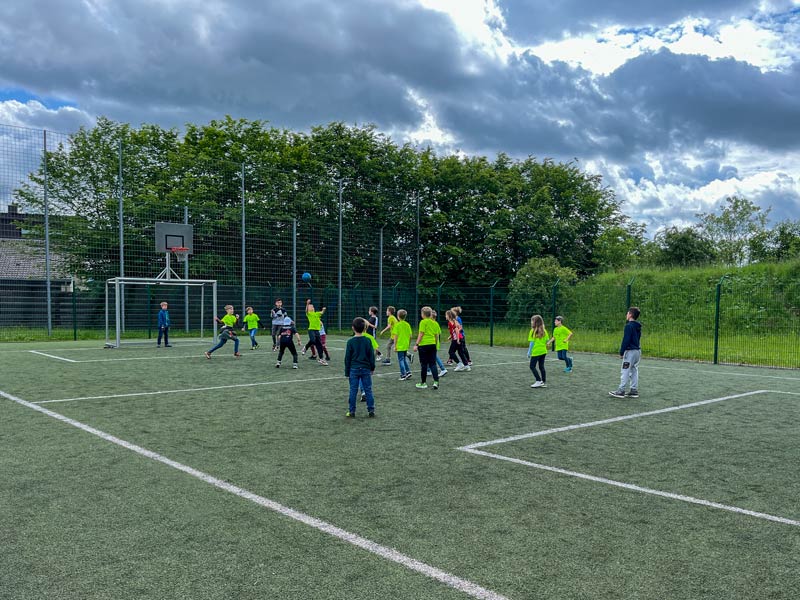 Kinder spielen draußen auf einem MINI-Fußballfeld mit einem Ball.