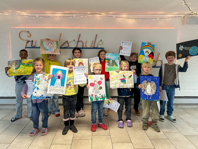 Gruppe von Kindern steht im Foyer mit hellen Fliesen, hält bunte Bastelarbeiten und Urkunden hoch, im Hintergrund ist der Schriftzug „Grundschule“.