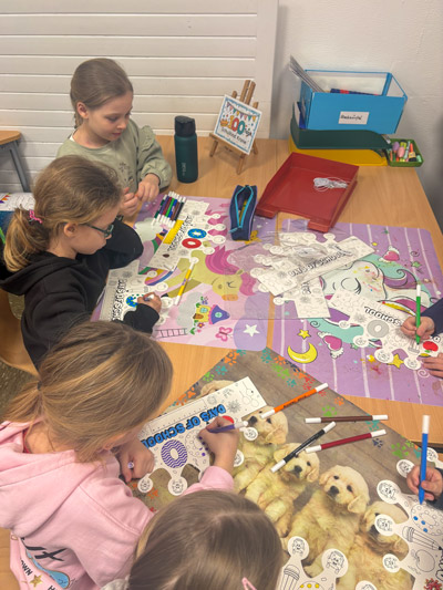 Vier Kinder sitzen an einem Tisch und malen auf großen Ausmalbildern mit bunten Stiften.