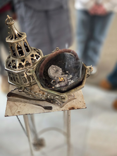 Räucherschale mit brennender Kohle auf einem Ständer vor unscharfem Hintergrund mit Personen.