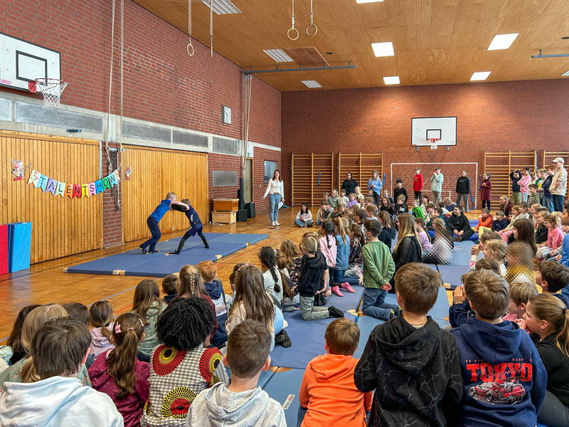 Zwei Kinder ringen auf einer Matte in einer Turnhalle vor sitzenden und stehenden Zuschauern.