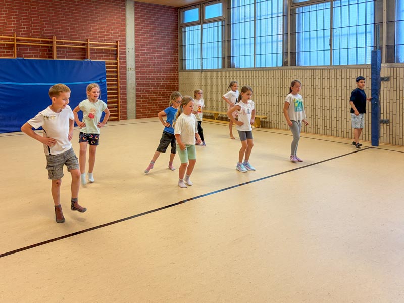 Kinder stehen in einer Turnhalle in zwei Reihen mit Händen in der Hüfte.