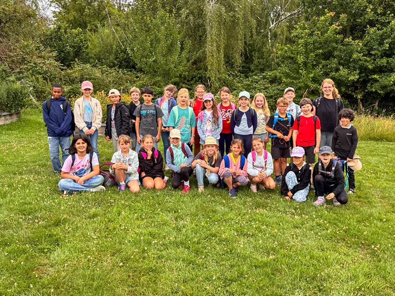 Gruppenfoto von Kindern und einer Erwachsenen auf einer Wiese vor Bäumen.